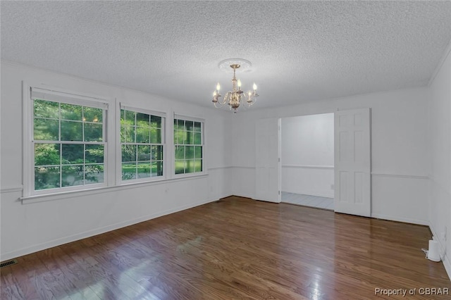 spare room with visible vents, a textured ceiling, wood finished floors, an inviting chandelier, and baseboards