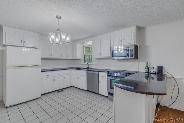 kitchen with appliances with stainless steel finishes, an inviting chandelier, sink, kitchen peninsula, and white cabinetry