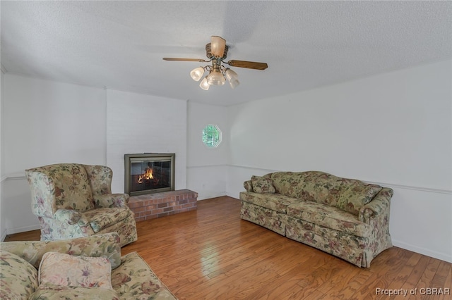 living room featuring ceiling fan, a fireplace, a textured ceiling, and hardwood / wood-style flooring