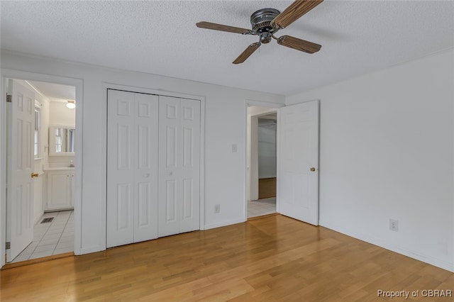 unfurnished bedroom featuring ensuite bathroom, a closet, light tile patterned floors, a textured ceiling, and ceiling fan