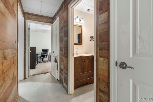 hallway with wood walls, a drop ceiling, and sink