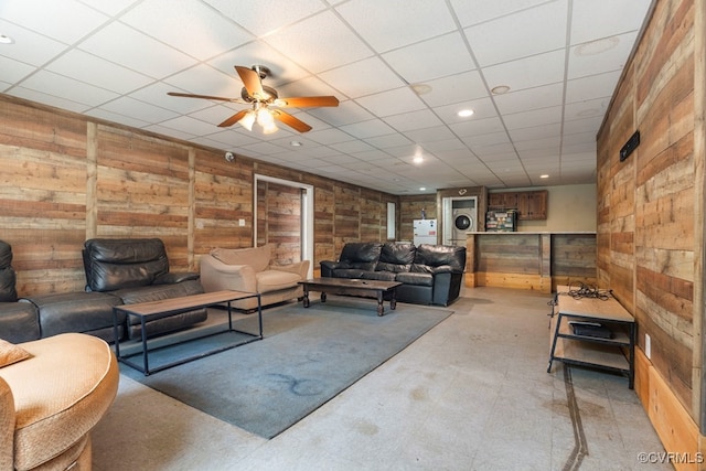 living room with wood walls, a drop ceiling, and ceiling fan