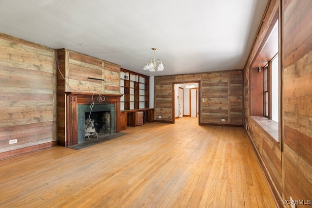 unfurnished living room featuring light wood-type flooring, wooden walls, and a notable chandelier