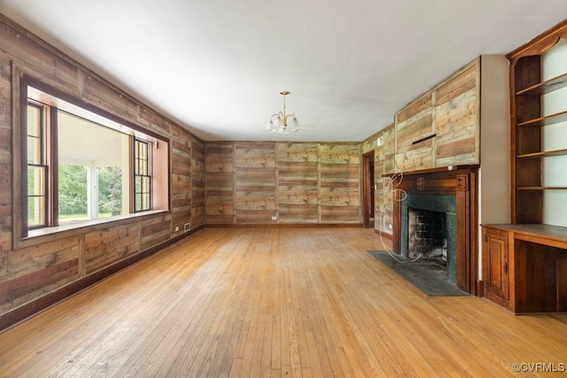 unfurnished living room featuring a notable chandelier, light hardwood / wood-style flooring, and wooden walls