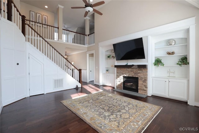 unfurnished living room featuring built in shelves, a stone fireplace, a high ceiling, and dark wood-type flooring