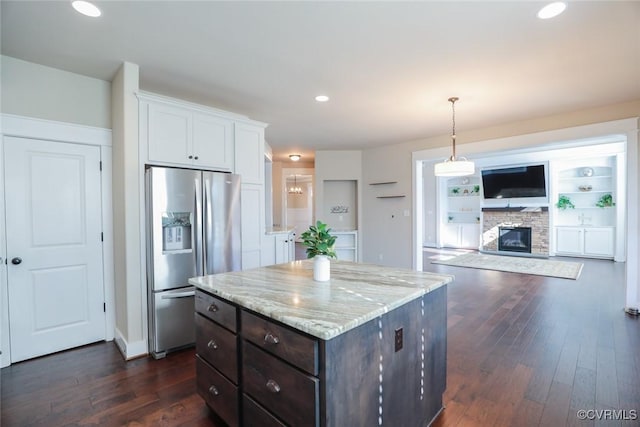 kitchen with a stone fireplace, stainless steel fridge with ice dispenser, white cabinets, decorative light fixtures, and dark brown cabinetry