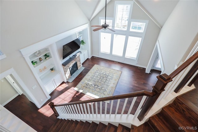 living room featuring a towering ceiling, ceiling fan, dark hardwood / wood-style floors, and a fireplace