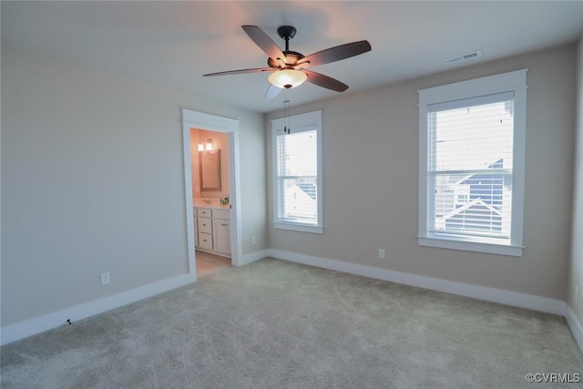 unfurnished bedroom with ceiling fan, light colored carpet, and ensuite bathroom