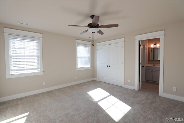 unfurnished bedroom featuring multiple windows, a closet, ensuite bath, and ceiling fan