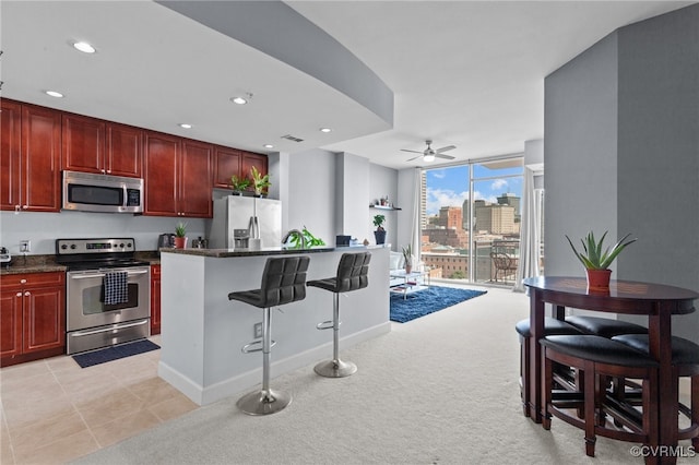 kitchen featuring a breakfast bar area, light carpet, appliances with stainless steel finishes, and ceiling fan