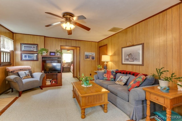 living room with ceiling fan, crown molding, light colored carpet, and wooden walls