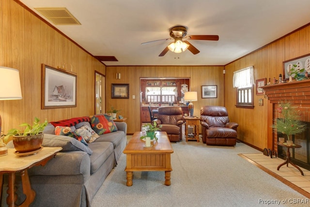 carpeted living room with ceiling fan, wooden walls, and a fireplace