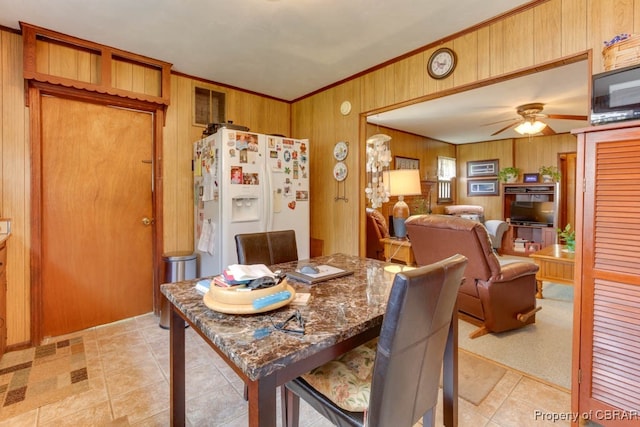 dining room with ceiling fan, wood walls, and light tile patterned floors