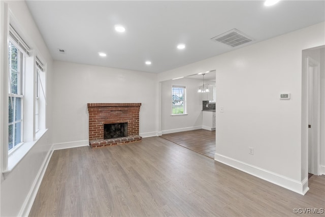 unfurnished living room featuring hardwood / wood-style floors, a notable chandelier, a brick fireplace, and a healthy amount of sunlight