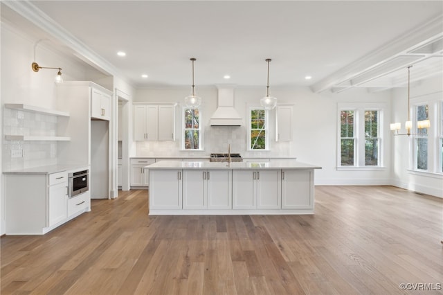 kitchen featuring custom exhaust hood, decorative backsplash, white cabinets, and light hardwood / wood-style floors