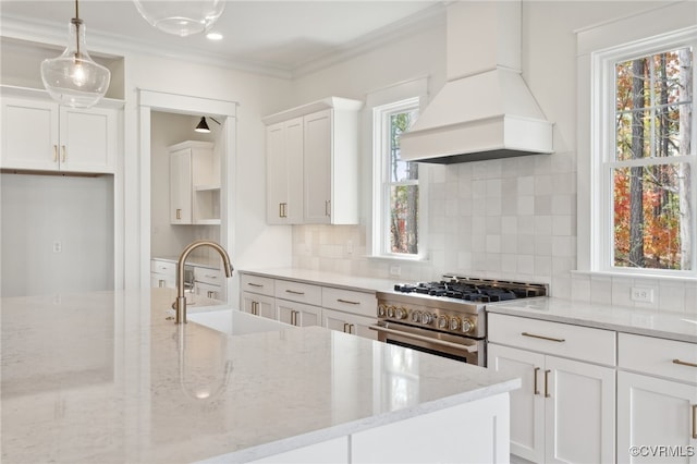 kitchen featuring high end stove, pendant lighting, white cabinets, custom range hood, and light stone counters