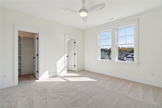 unfurnished bedroom featuring light carpet, a walk in closet, a closet, and ceiling fan