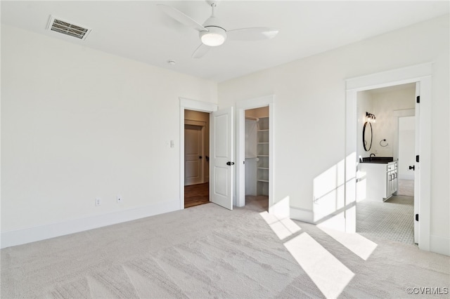 unfurnished bedroom with light carpet, a walk in closet, a closet, and ceiling fan