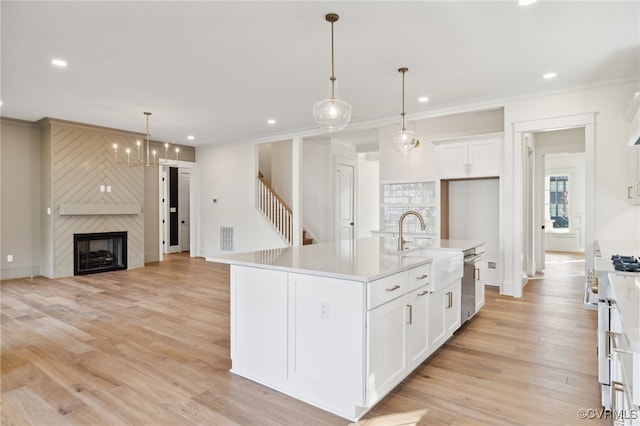 kitchen with white cabinets, a kitchen island with sink, light wood-type flooring, a fireplace, and pendant lighting