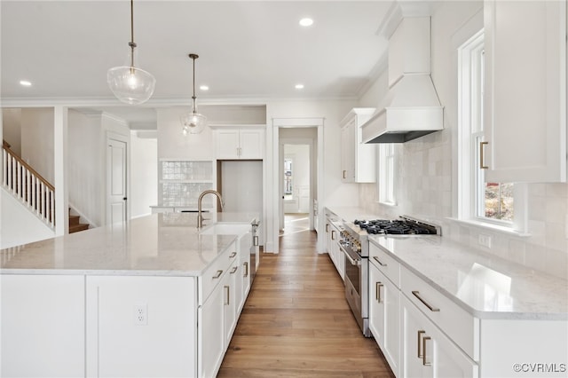 kitchen with light stone countertops, decorative light fixtures, a center island with sink, and high end range