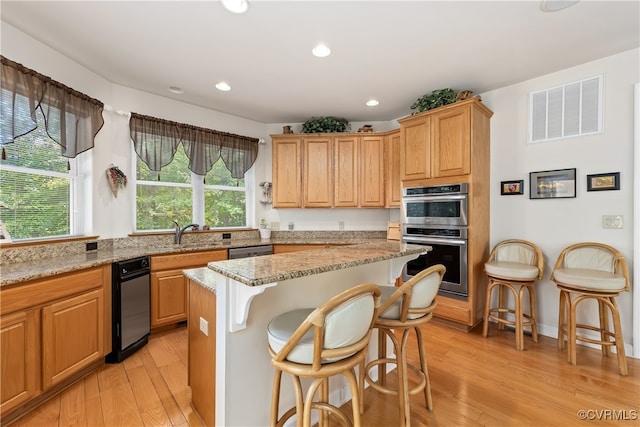 kitchen with a kitchen island, light hardwood / wood-style flooring, appliances with stainless steel finishes, a breakfast bar, and light stone countertops