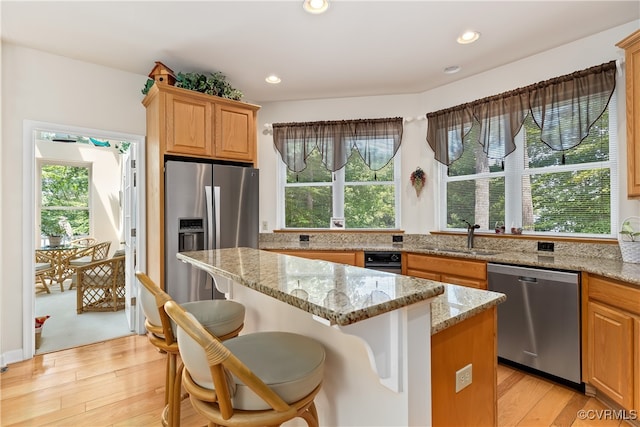 kitchen with a sink, a center island, light stone countertops, and stainless steel appliances