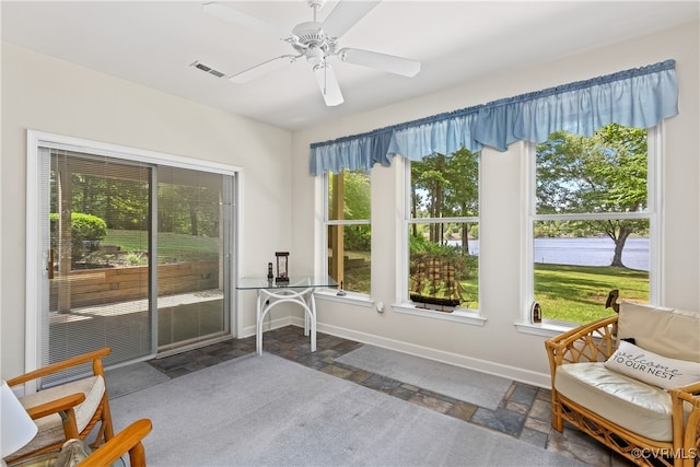 living area featuring ceiling fan, baseboards, visible vents, and stone tile flooring