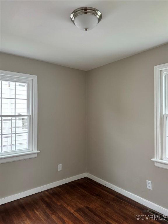 empty room featuring visible vents, dark wood-type flooring, and baseboards