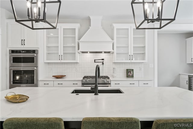 kitchen featuring custom range hood, stainless steel appliances, hanging light fixtures, and white cabinetry