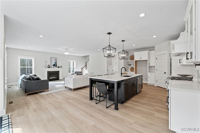 kitchen featuring hanging light fixtures, a kitchen island with sink, white cabinets, light wood-type flooring, and sink