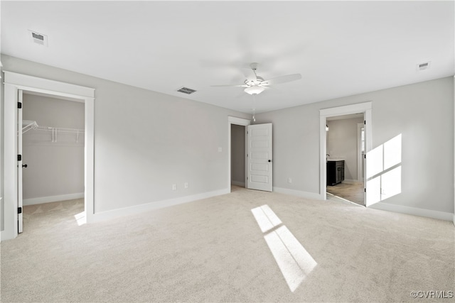 unfurnished bedroom featuring light colored carpet, ceiling fan, a spacious closet, a closet, and connected bathroom