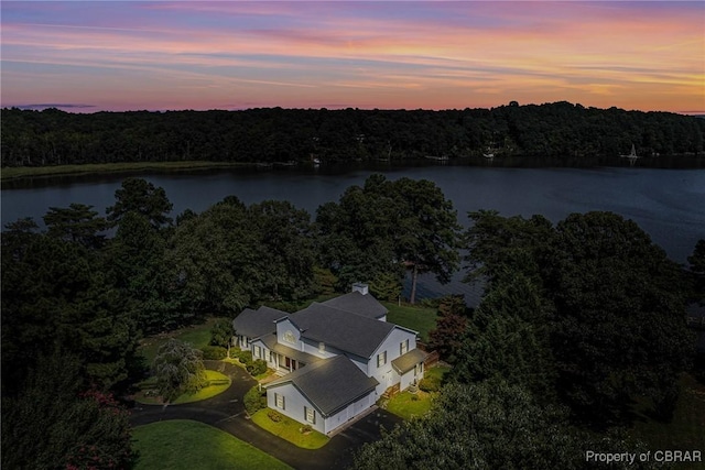 aerial view at dusk featuring a forest view and a water view