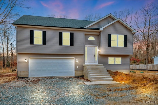 raised ranch featuring a garage, fence, driveway, and a shingled roof