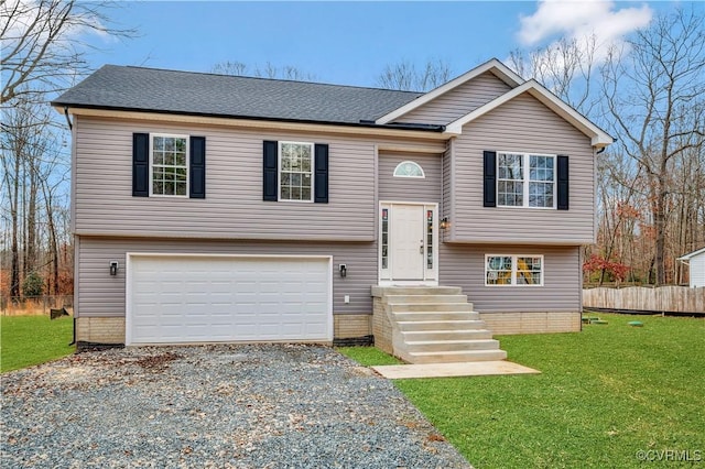 raised ranch with gravel driveway, roof with shingles, a front yard, fence, and a garage