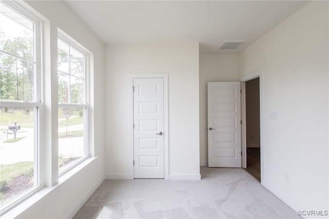 unfurnished bedroom featuring light colored carpet, visible vents, baseboards, and multiple windows