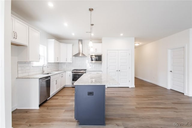 kitchen with a kitchen island, a sink, white cabinets, appliances with stainless steel finishes, and wall chimney exhaust hood