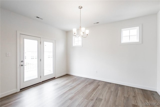 unfurnished room featuring a chandelier, light wood-type flooring, visible vents, and baseboards