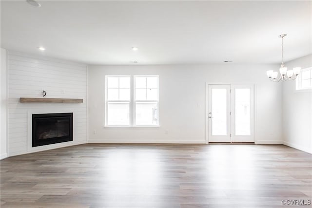 unfurnished living room featuring a large fireplace, a notable chandelier, baseboards, and wood finished floors