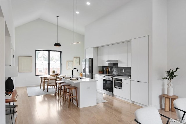 kitchen with stainless steel appliances, a kitchen island with sink, pendant lighting, high vaulted ceiling, and white cabinetry