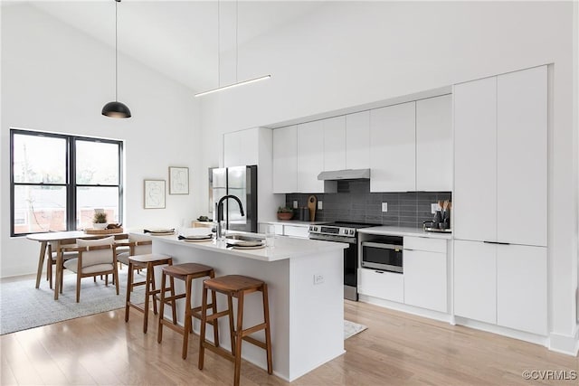 kitchen featuring tasteful backsplash, stainless steel appliances, pendant lighting, high vaulted ceiling, and white cabinets