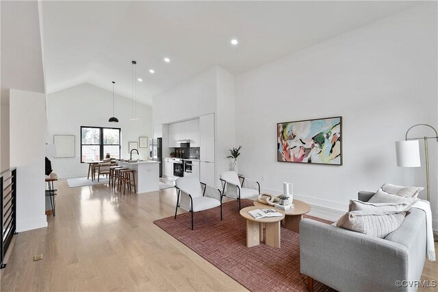 living room featuring sink, high vaulted ceiling, and light wood-type flooring