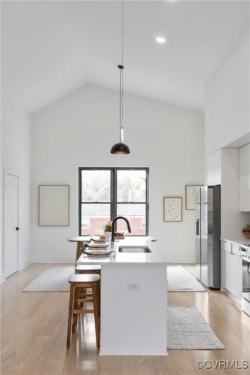 kitchen with sink, hanging light fixtures, high vaulted ceiling, stainless steel fridge, and white cabinets