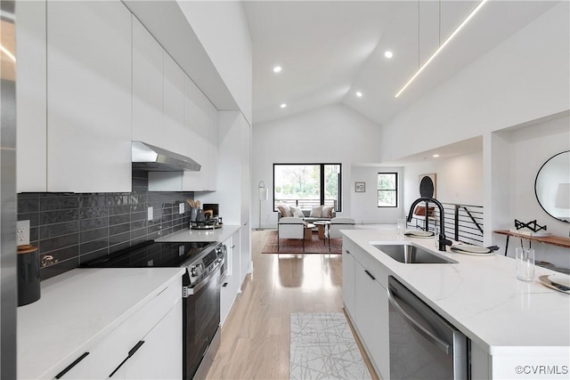 kitchen with high vaulted ceiling, wall chimney range hood, sink, white cabinetry, and stainless steel appliances