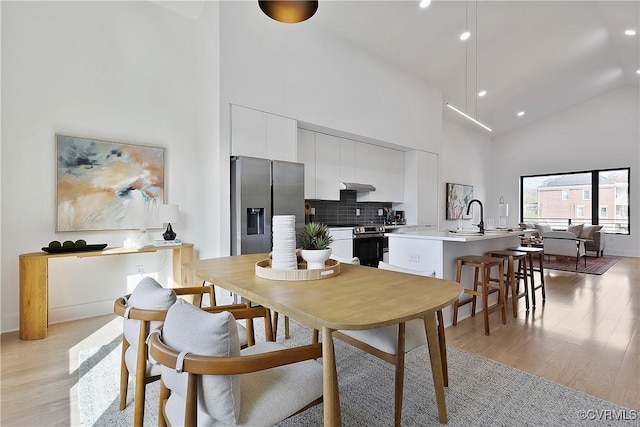 dining area featuring sink, high vaulted ceiling, and light hardwood / wood-style floors