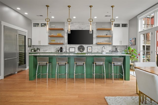 kitchen with light wood-type flooring, white cabinetry, a center island with sink, and hanging light fixtures