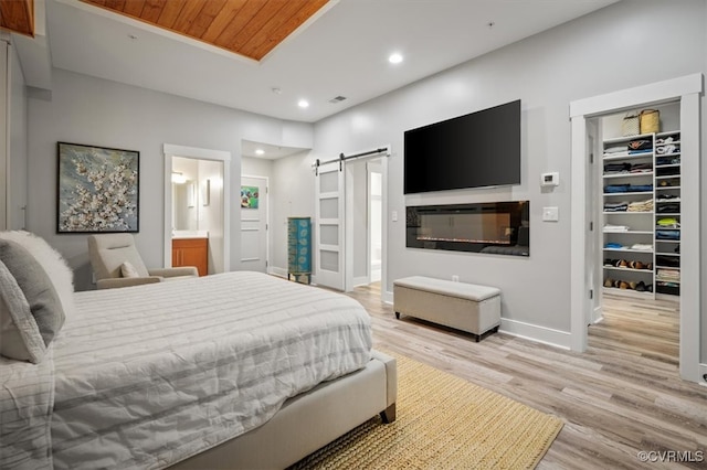 bedroom featuring a barn door, light wood-type flooring, wood ceiling, a walk in closet, and connected bathroom