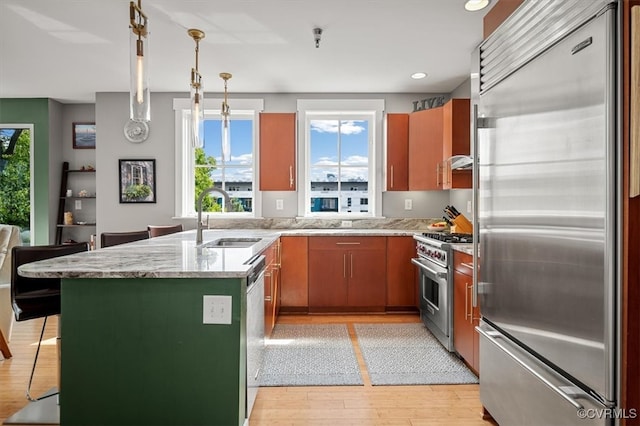 kitchen featuring pendant lighting, sink, light stone counters, light wood-type flooring, and premium appliances