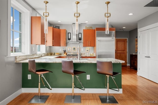 kitchen with light wood-type flooring, pendant lighting, built in refrigerator, and a kitchen bar