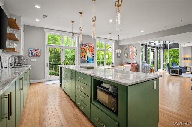 kitchen with green cabinetry, light stone counters, light hardwood / wood-style floors, sink, and a kitchen island