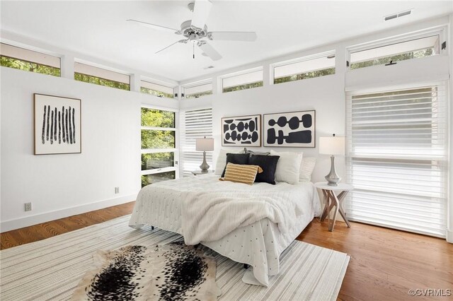 bedroom with ceiling fan, wood-type flooring, and multiple windows